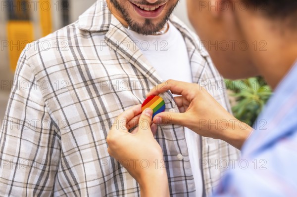 Gay partner pinning a rainbow pride badge to their partner's plaid shirt, close up of hands showing love, support and lgbtq plus inclusion, unity and celebration