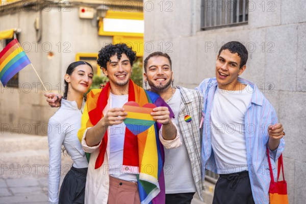 Diverse group of young adults smiling and celebrating pride in the city, holding a rainbow heart and small pride flag, expressing joy, solidarity, and inclusion outdoors