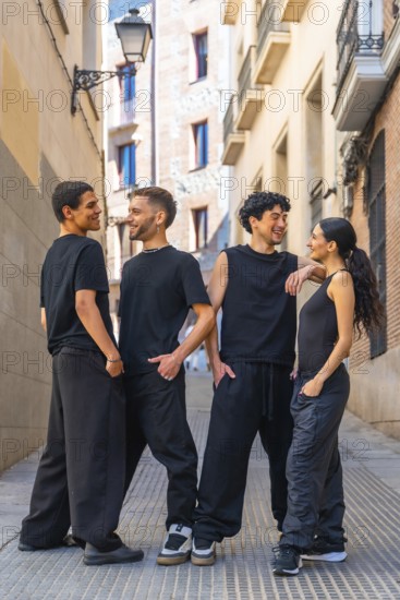 Four diverse young friends wearing black casual clothing are happily interacting, smiling, and talking while standing together in an urban alley or street