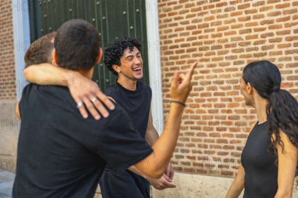 Group of diverse young adult friends embracing, laughing, and gesturing while enjoying a lively conversation together on a city street in front of a brick wall and a green door