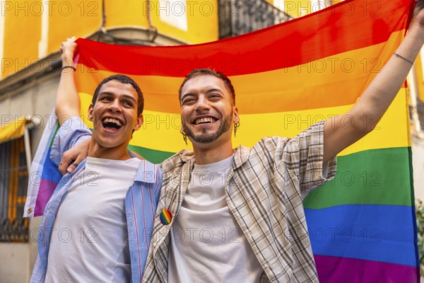 Happy young gay couple smiling, celebrating love, diversity, and lgbtq plus rights, holding a vibrant rainbow flag during a pride event on an urban street