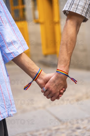 Couple's hands holding together, both wrists featuring rainbow bracelets, symbolizing love, pride, and support for the lgbtq plus community, representing equality