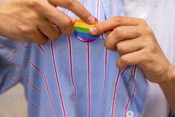 Person's hands carefully pinning a rainbow pride flag button onto a blue and white striped shirt, symbolizing support for lgbtq plus community, identity, and acceptance