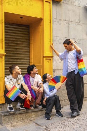 Group of four diverse friends celebrating lgbtq plus pride in the city, waving rainbow flags and a fan, smiling and showing unity, joy, acceptance and youthful solidarity