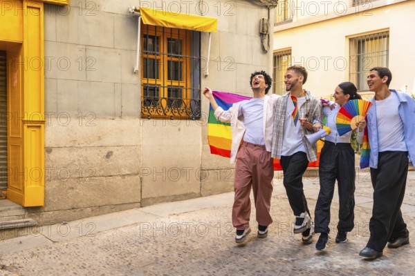 Happy queer friends celebrating lgbtq pride on a sunny historic cobblestone street in madrid, holding a rainbow flag, fan and megaphone, smiling, united and joyful
