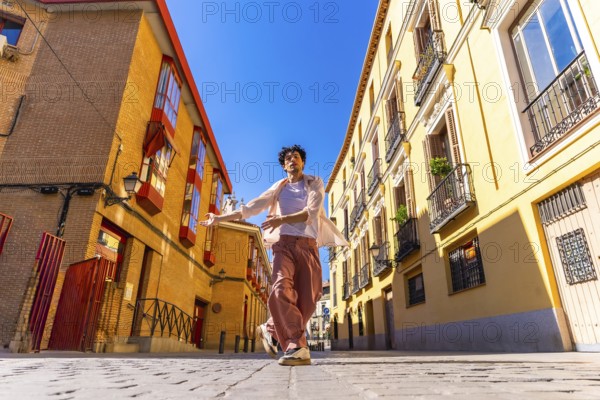 Young man freely dancing in a cobblestone street between traditional architecture buildings under a bright blue sky, moving with joy and expressing freedom
