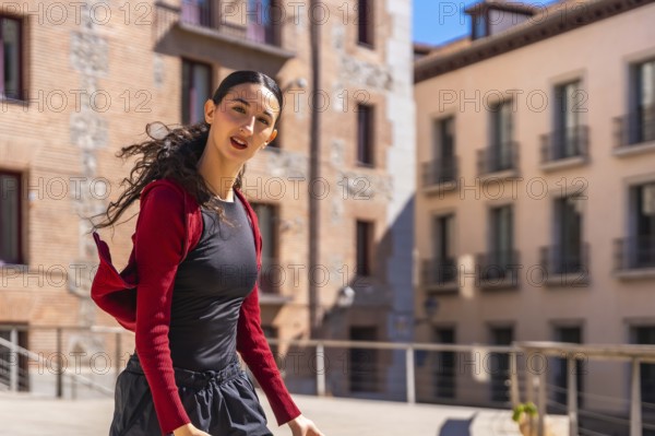 Hispanic young woman dancing with energy and spirit in an urban street, expressing freedom and joy in movement, with traditional architecture in the background