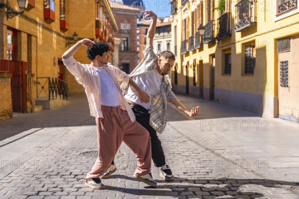Two young men performing energetic contemporary street dance on cobblestones in madrid, expressing freedom, connection and joy under bright summer sunlight in an urban cityscape