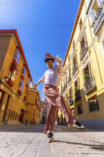 Young man dancer performing a dynamic street dance move in a vibrant old city urban setting under a clear blue sky, showing energy and freedom of expression