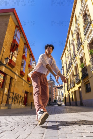 Young man striking a dynamic urban dance pose on sunlit cobblestones in madrid, radiating energy, style and carefree expression against historic city architecture