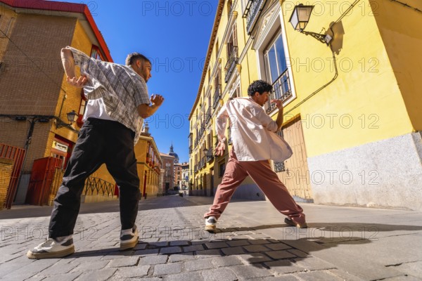 Two young men expressing themselves through street dance movement, performing a modern hip hop choreography on a cobblestone road in an old european city street under bright sunlight