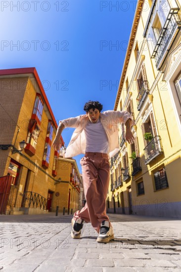 Stylish young man with intense expression executing a dynamic street dance move on cobblestones in a vibrant european city district, full length, sunny, energetic summer scene