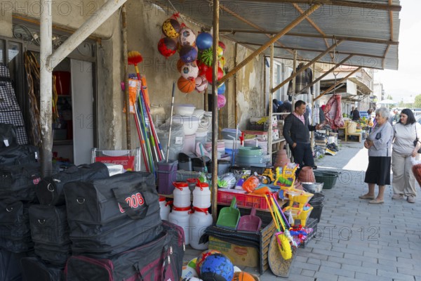 A shopping street with toys and household goods, meat hanging in front of the door, customers looking at the goods, Martuni, Gegharkunik province, Armenia