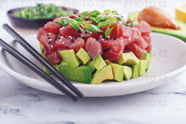 Fresh tuna tartare with avocado served on a marble table with soy sauce and seaweed salad