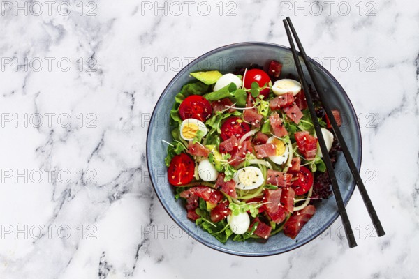 Salad with fresh tuna, cherry tomatoes and quail eggs and avacado, served with chopsticks