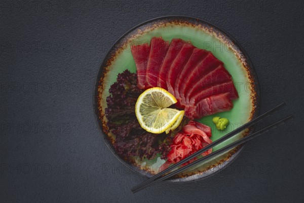 Fresh tuna sashimi served with lemon, wasabi, and pickled ginger on a dark background