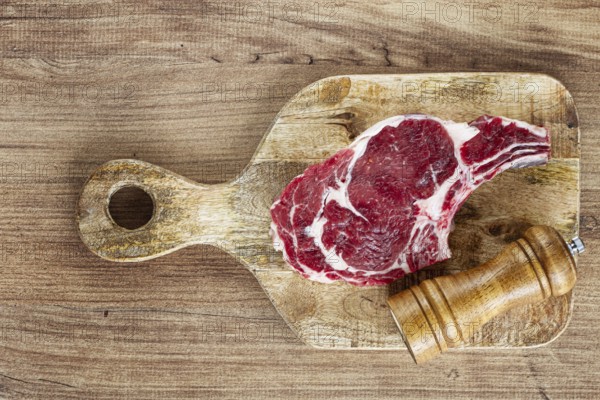 Raw rib eye steak, cowboy steak, on a wooden chopping board, top view, no people