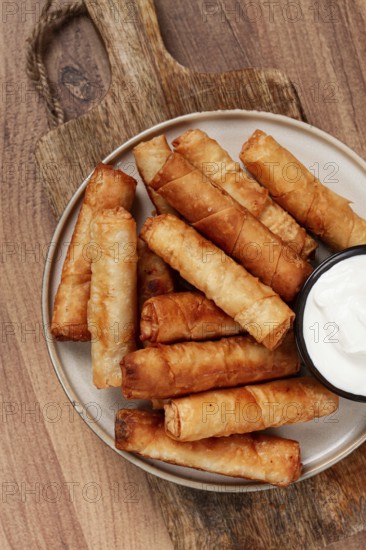 Fried spring rolls with cheese, on a wooden background, with cream sauce, no people