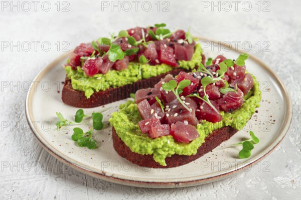 Toasts with fresh tuna and avocado, spread on black bread and sprinkled with microgreens, breakfast, healthy food