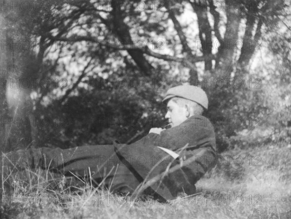 Image of pensive young man lying in countryside field with trees c 1910-1920