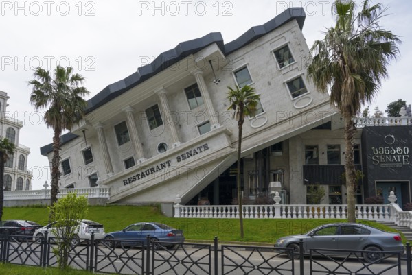 A leaning building with a restaurant in an urban environment, surrounded by palm trees and parked cars, Senate Restaurant and Lounge, Batumi, Black Sea, Adjara region, Adjara, Autonomous Republic of, Georgia