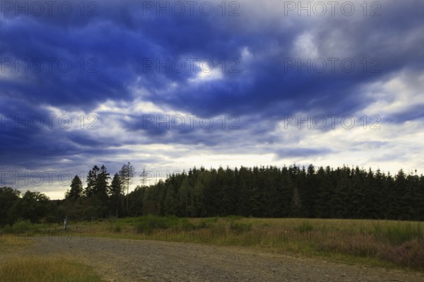 Dramatic sky with dark clouds over a field and neighbouring forest, heaths and rough grassland nature reserve near Trupbach, Siegen