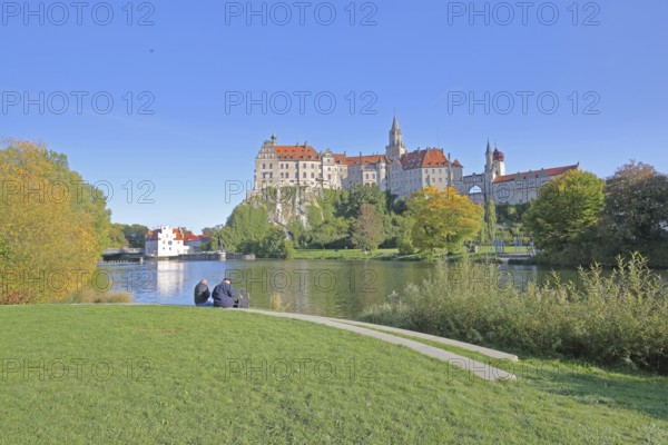 Hohenzollern Castle and Danube, river bank with autumn colours and two seated people, landmark, castle, Sigmaringen, Swabian Alb, Baden-Württemberg, Germany