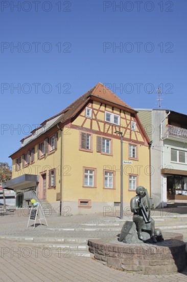 Sculpture Minnesänger von Wissenlo by the sculptor Hatto Zeidler 1978 and Bronner House, monument, bronze sculpture, seated harp player with town coat of arms, musician with harp playing music, seated, coat of arms shield, Unterer Markt, Wiesloch, Baden-Württemberg, Germany