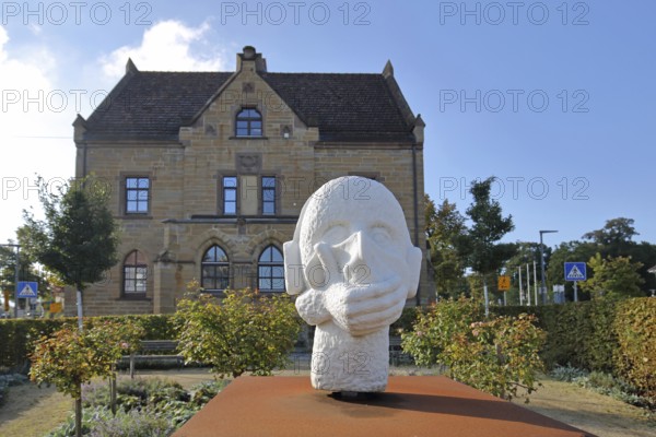 Sculpture head with headphones and hand for in front of the mouth, ambivalent symbolism for peace, silence and listening to music, no, not, communication, being alone, speaking, listening to music, music, listening, listening, mouth protection, hearing protection, contradiction, contradictory, house, Zollerschule, Hechingen, Swabian Alb, Baden-Württemberg, Germany