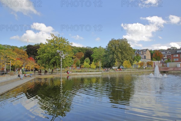 Bastinsweiher with sculpture, seating, bench, people, pedestrians, park, pond, autumn colours, fountain, water jet, Rhineland, Stolberg, North Rhine-Westphalia, Germany