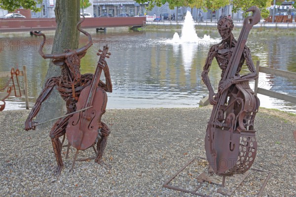 Sculpture The Concert by Günther Fahrner, rusty, metal sculpture, sheet metal, modern art, two bizarre whimsical musicians, duet, double bass player, cello player, string instruments, cello, double bass, make music, musician, pond, beach, shore, bull figure, Bastinsweiher, Rhineland, Stolberg, North Rhine-Westphalia, Germany