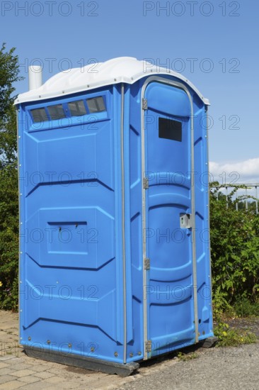 Blue and white portable chemical toilet temporarily installed by the roadside for public use in summer, Quebec, Canada