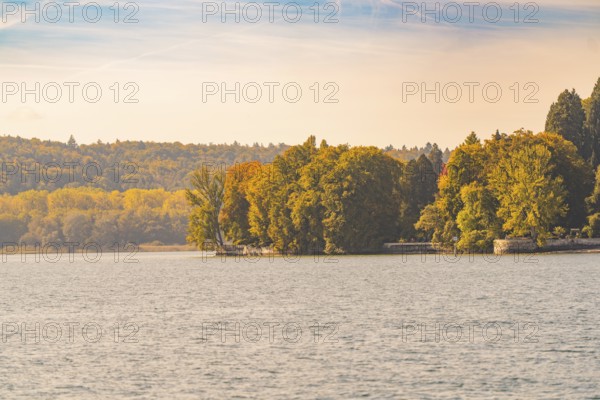 Autumnal shoreline with trees and calm lake, Mainau Island, Lake Constance, Germany