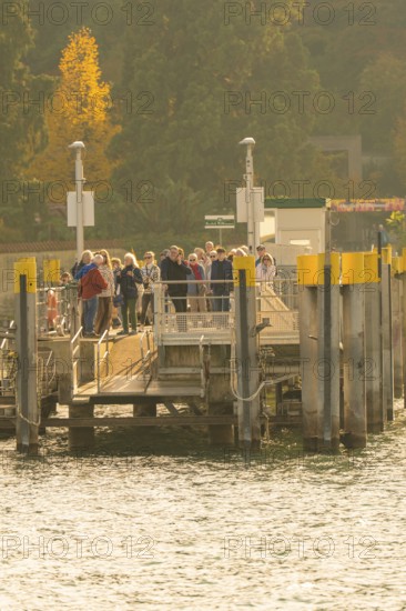 People waiting at a jetty surrounded by trees with autumn colours, Mainau Island, Lake Constance, Germany