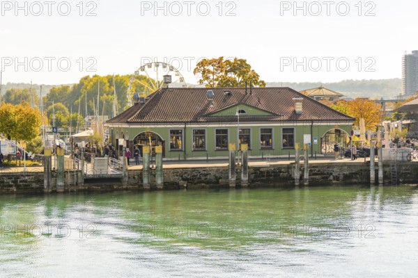 A building at the harbour with autumnal vegetation and a Ferris wheel in the background in a cityscape, Constance, Lake Constance, Germany