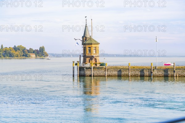 A picturesque harbour with a lighthouse, quietly situated on a clear water with houses in the background, Constance, Lake Constance, Germany