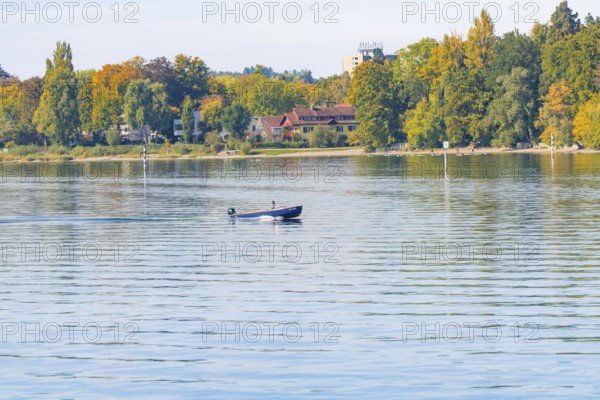 A boat sails across a calm lake surrounded by autumn trees, Constance, Lake Constance, Germany