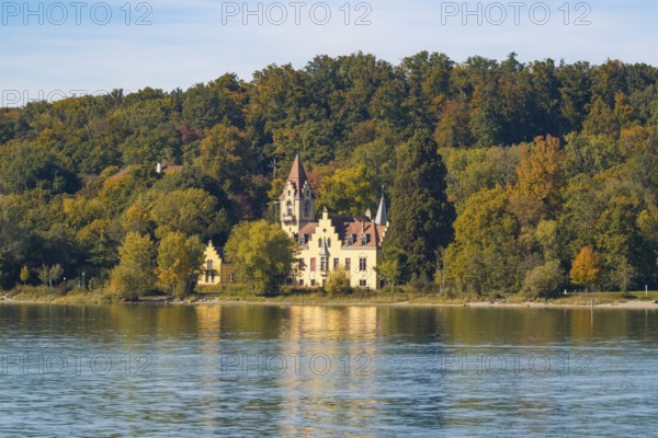 A picturesque castle on the shore of a lake surrounded by autumnal trees with a clear sky, Constance, Lake Constance, Germany