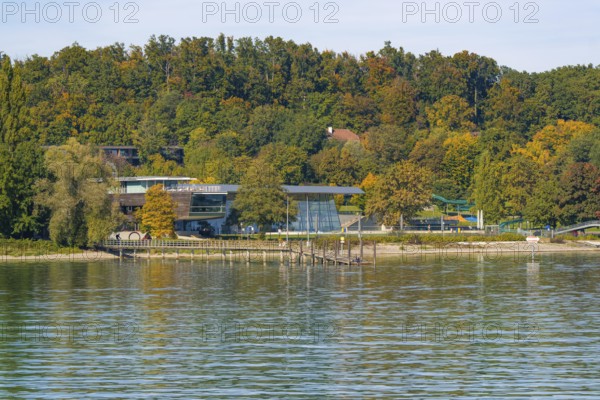 Modern building on the shore of a lake, surrounded by autumnal trees and a pier, Constance, Lake Constance, Germany