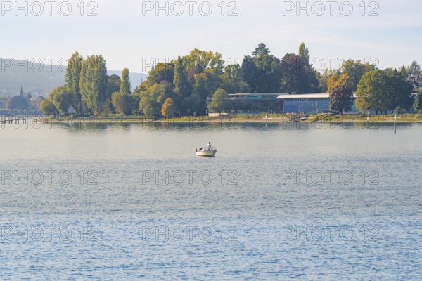 Small boat on a lake with autumn trees on the shore under a clear sky, Constance, Lake Constance, Germany
