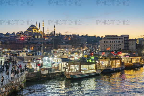 Restaurant boats on the shore of Eminönü, Rüstem Pasha Mosque and Suleymaniye Mosque at dusk, Istanbul, Turkey