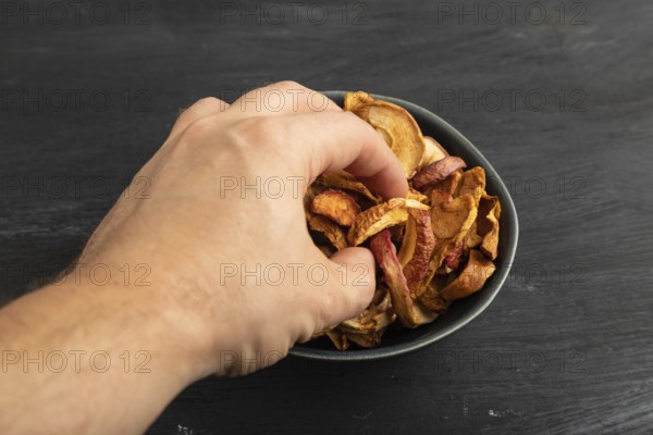 Dried Apples in ceramic bowl with hand on black wooden background. Side view, close up. healthy food, minimalism. sweet hold