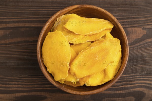 Dried Mango in wooden bowl on brown wooden background. Top view, close up, flat lay. healthy food, minimalism