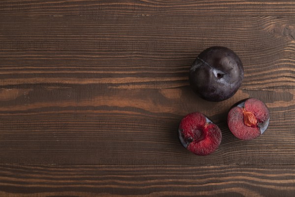 Purple Plum Cut in half on brown wooden background. Top view, flat lay, copy space. healthy food, vegetable, minimalism