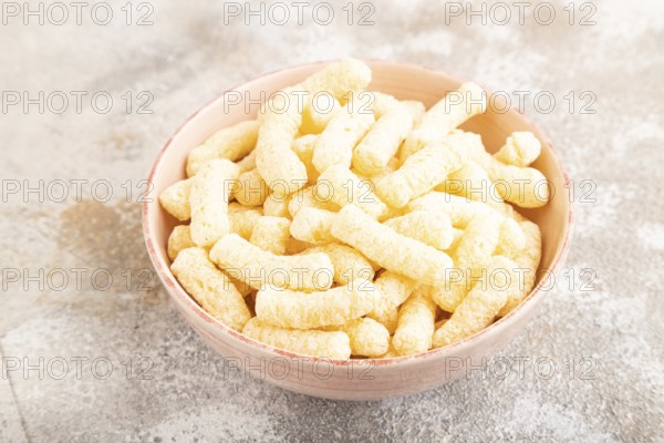 Corn flakes sticks with caramel in ceramic bowl on gray concrete background. Side view, close up