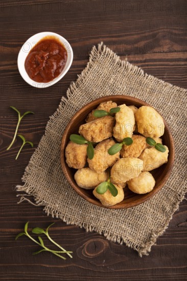 Fried crispy Chicken Nuggets with ketchup, microgreen on brown wooden background and linen textile. top view, flat lay, close up