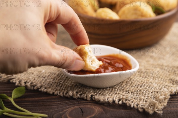 Fried crispy Chicken Nuggets with ketchup, microgreen on brown wooden background and linen textile with hand. side view, close up, selective focus