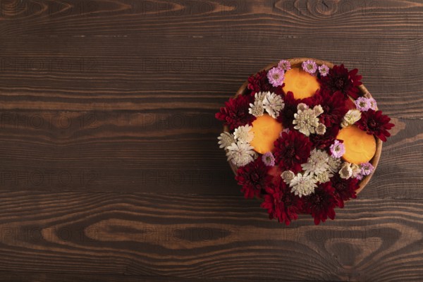 Wooden bowl with carrot slices and red Chrysanthemum flowers, Astrantia flowers, flower salad on brown wooden background, top view, flat lay, copy space, minimalism