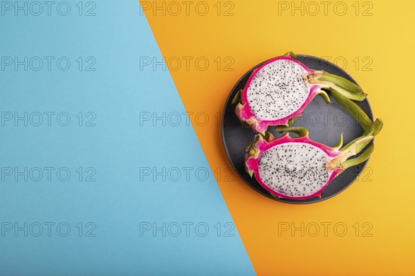 Ripe Pitaya on blue plate on blue and orange pastel paper background, top view, flat lay, copy space, minimalism
