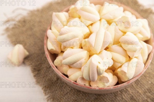 Orange and pink marshmallow in ceramic bowl on white wooden background, side view, close up, minimalism, selective focus